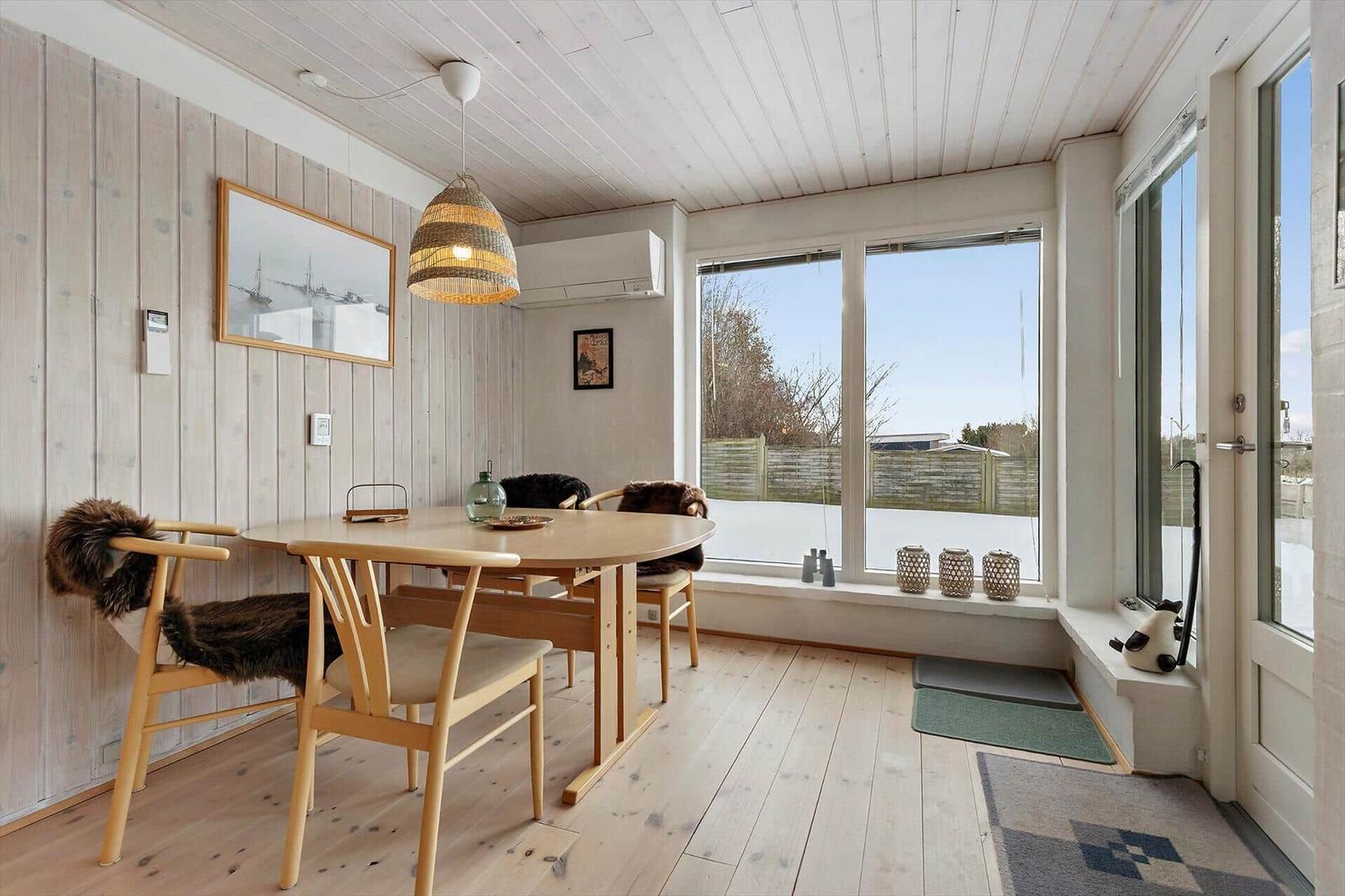 Dining room with wooden table, chairs, and large window. Outside is snow-covered.