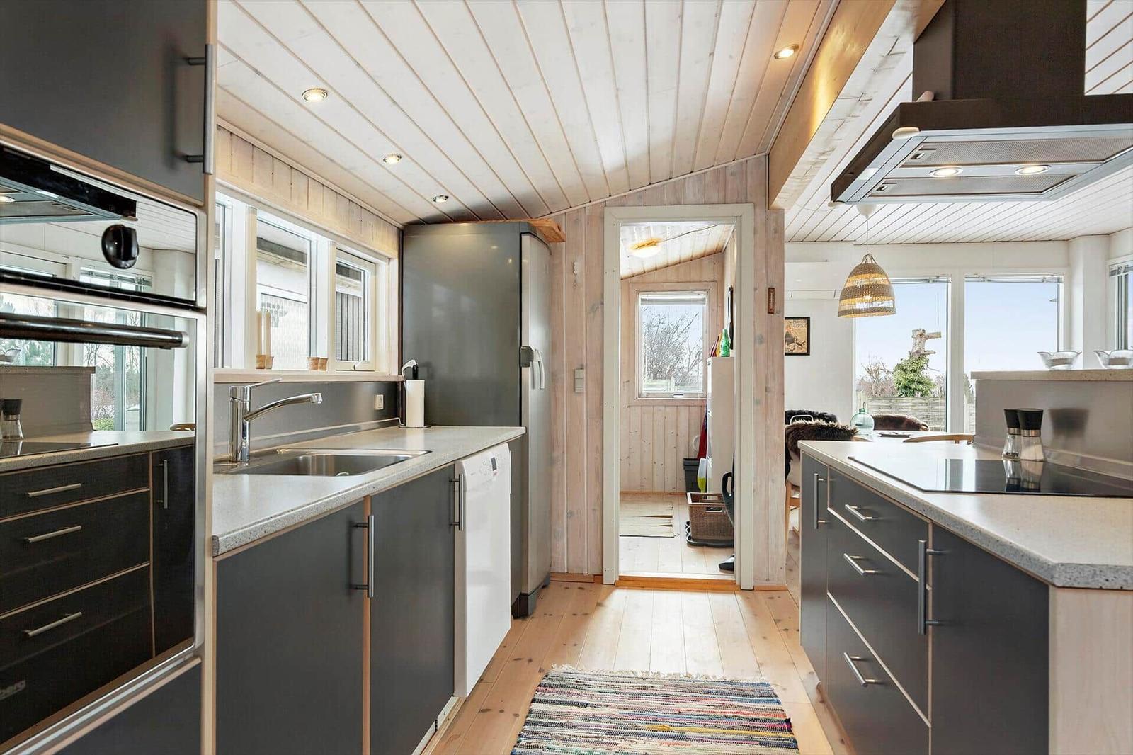 Kitchen with gray cabinets, stainless steel sink, and wooden floor. Corridor to living area.