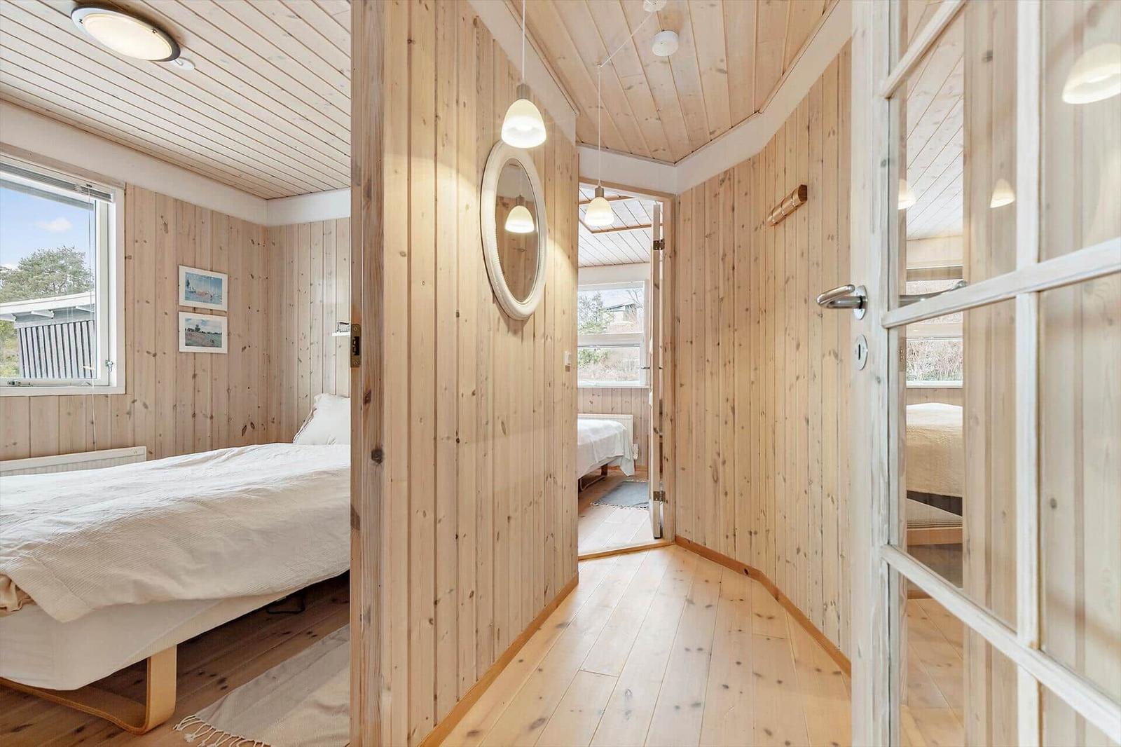 Bedroom with wooden walls, bed, and window. Hallway with mirror and door to other rooms.