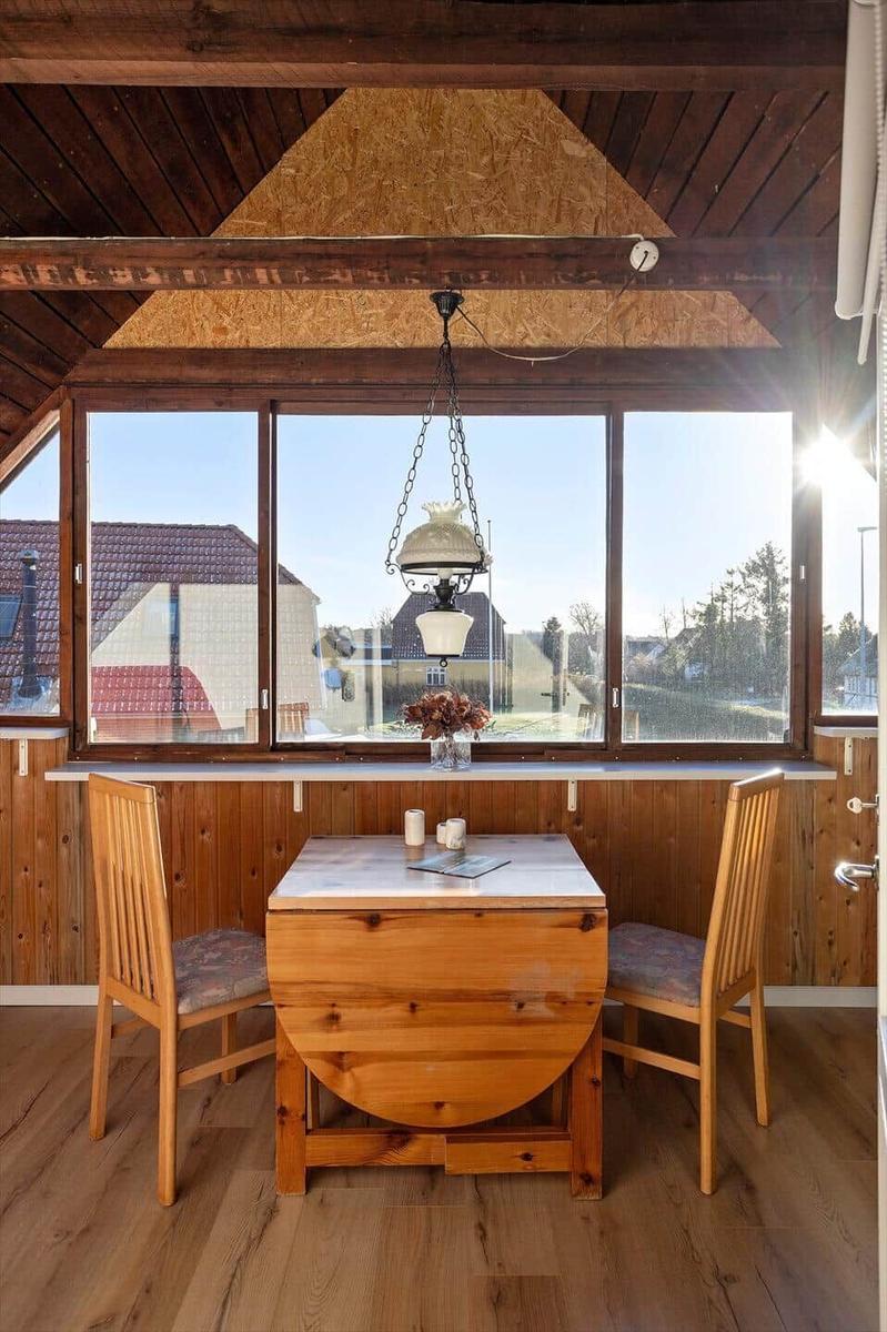 Dining room with wooden table, two chairs, and large window. Wooden ceiling and floor.