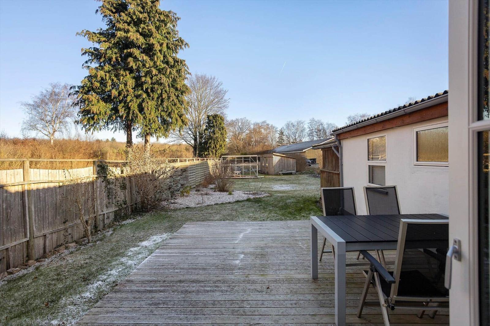 Deck with table and chairs, view of garden and house.