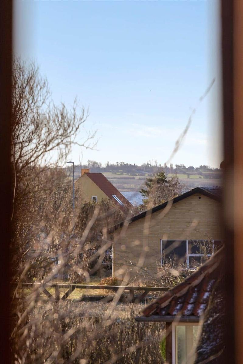 View from a window shows a house with a red roof and a lake in the background.