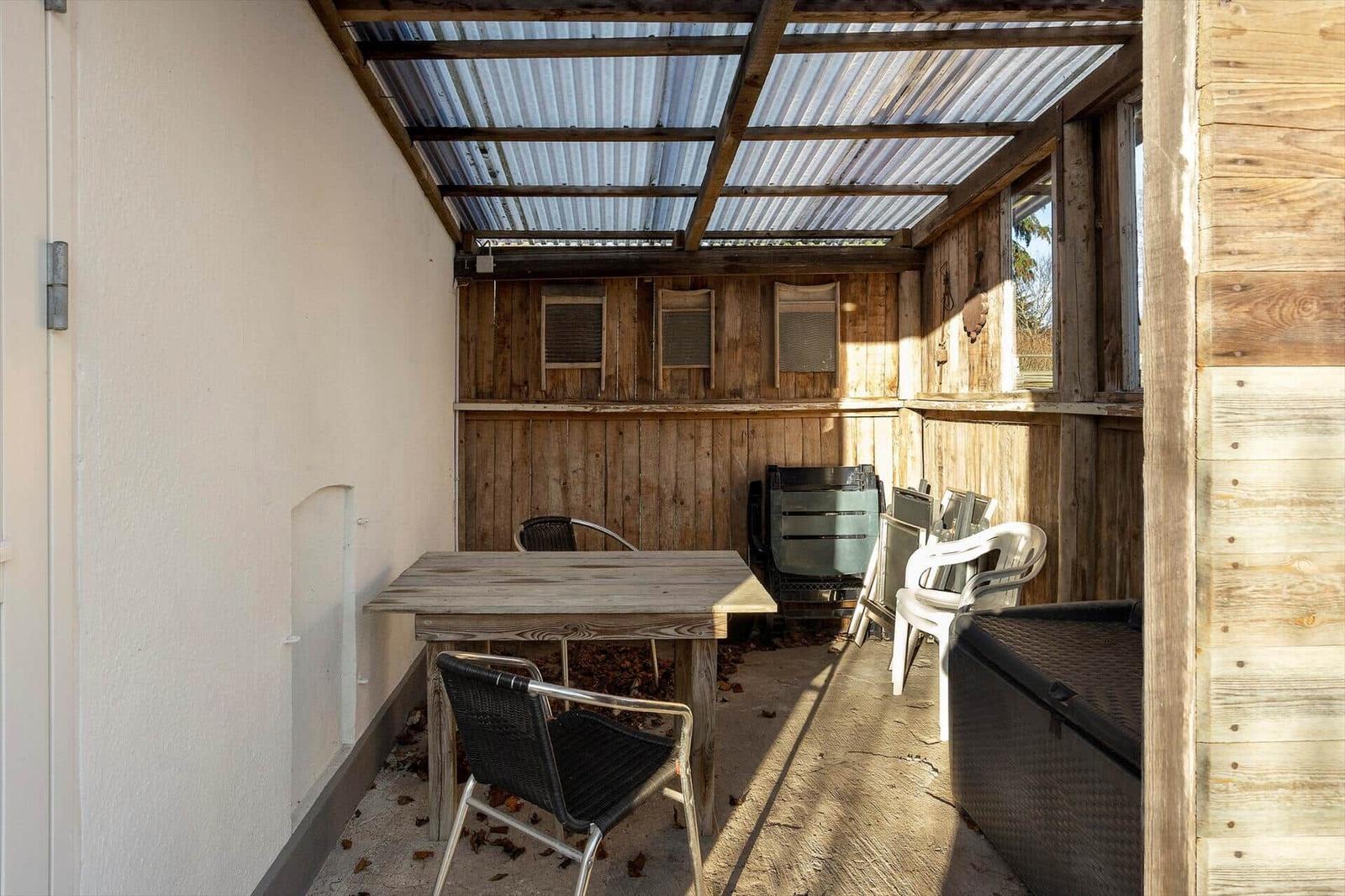 Covered outdoor area with table, chairs, and wooden wall.
