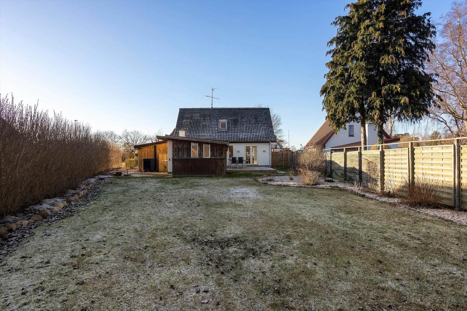 House with garden, terrace, and wooden garage. Lawn with frost. Tall tree on the right.