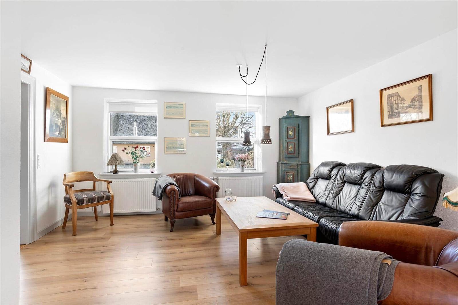 Living room with wooden floor, sofa, chairs, and table. Pictures hang on the walls.