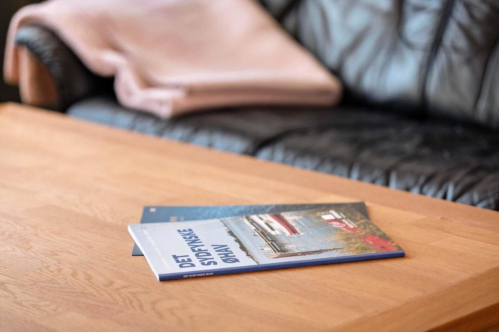 A book rests on a wooden table in front of a sofa with a blanket.