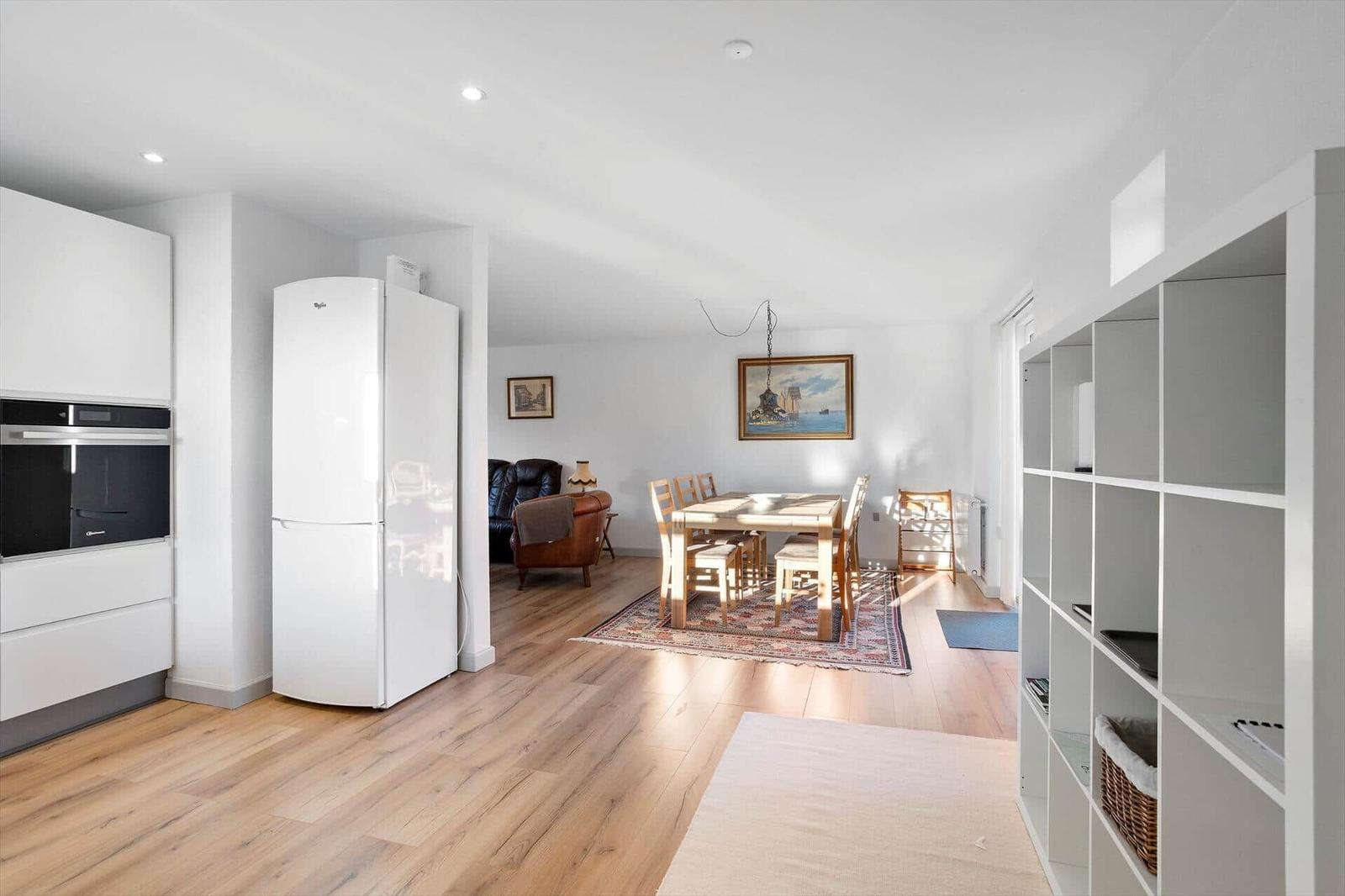 Kitchen with fridge and oven. Dining area with table and chairs. Living area with leather sofa.