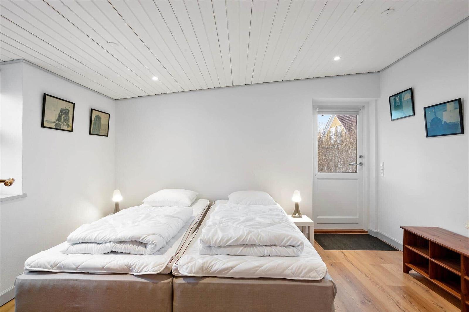 Two sleeping areas with white bedding, wooden floor, and white walls.