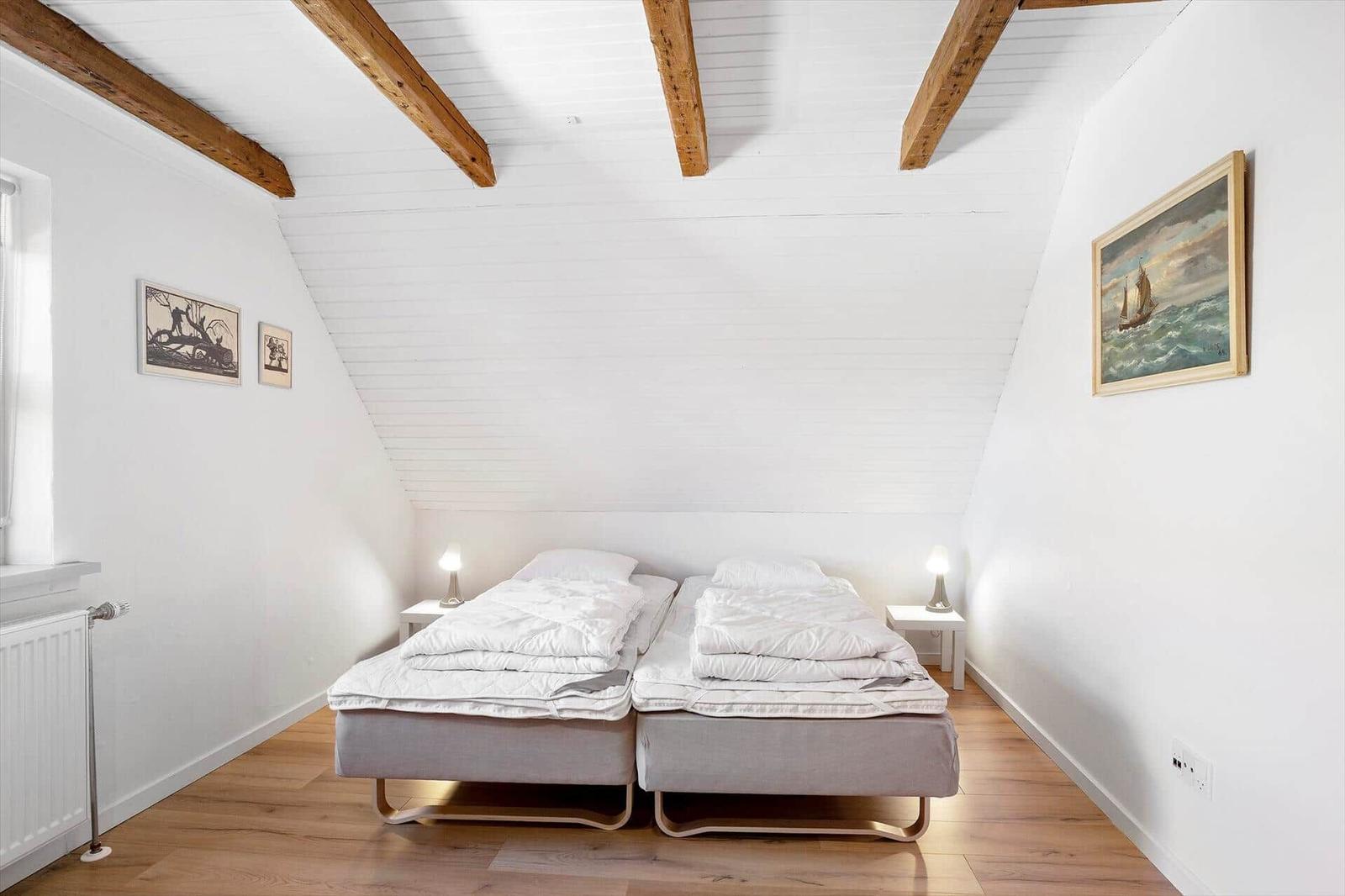 Two beds in an attic room with wooden beams and wall pictures.