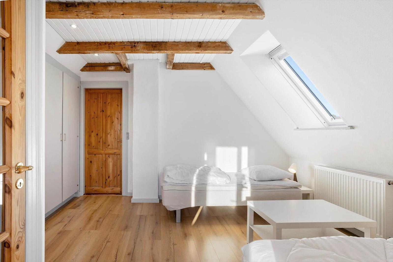 Bedroom with sloped ceiling, wooden beams, skylight, and two beds.
