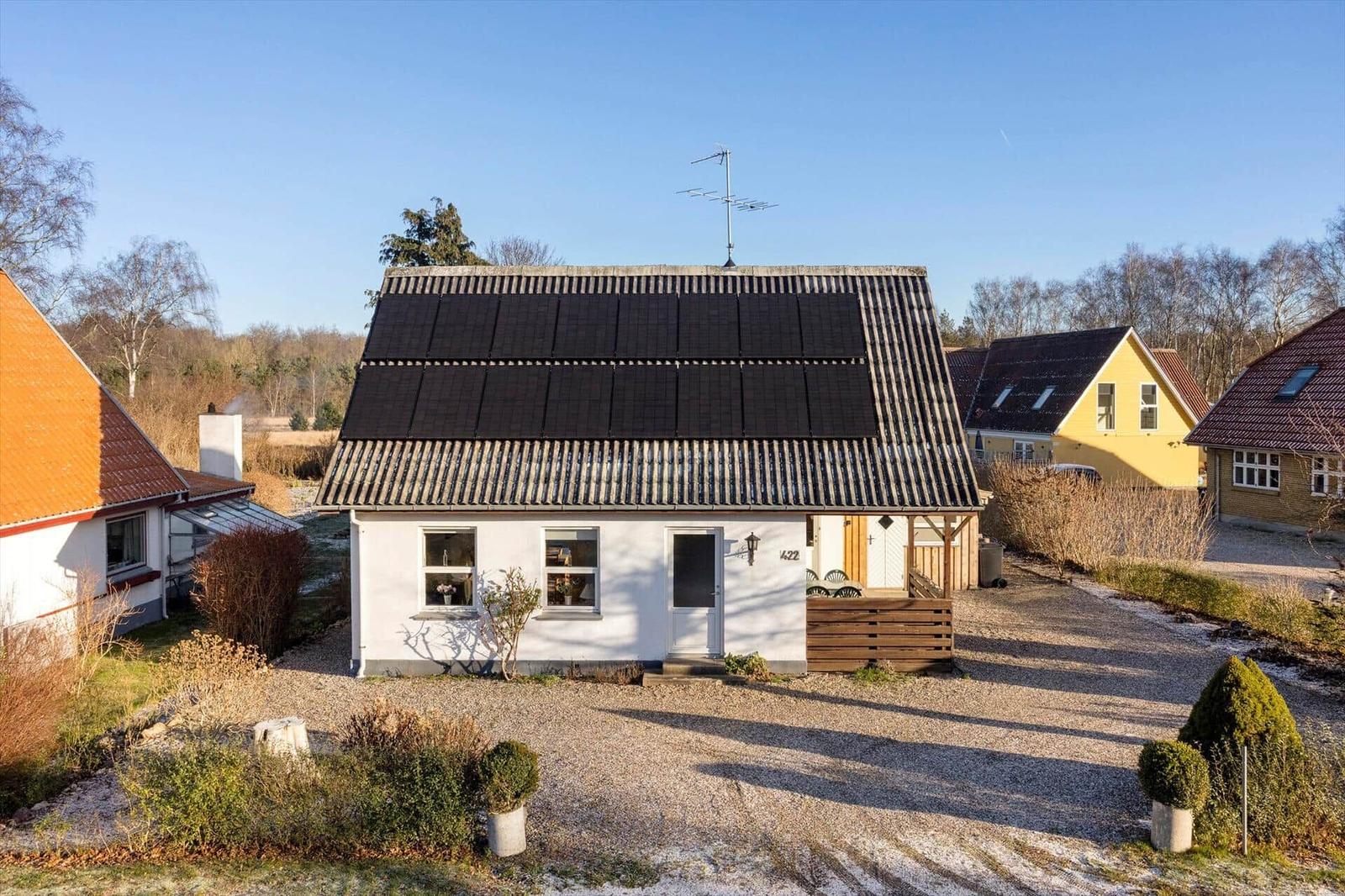 A white house with solar panels on the roof, garden, and neighboring houses.