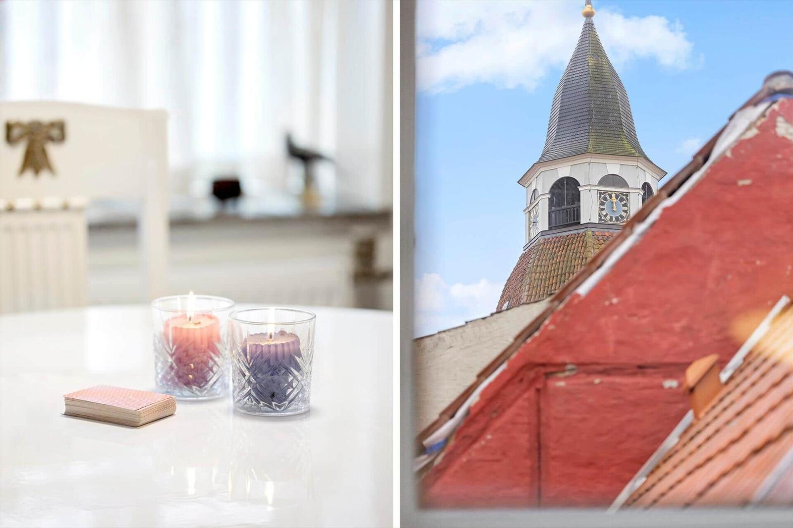Table with lit candles and playing cards. View of church tower with red roof.