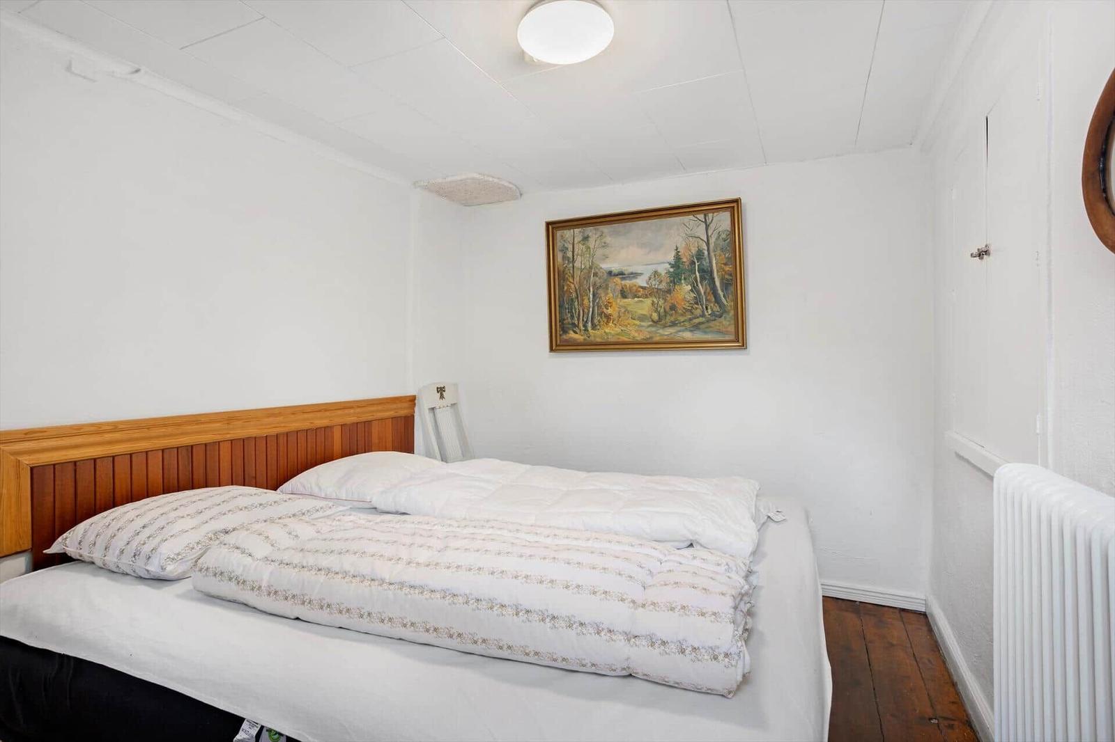A bedroom with bed, wall painting, and radiator.