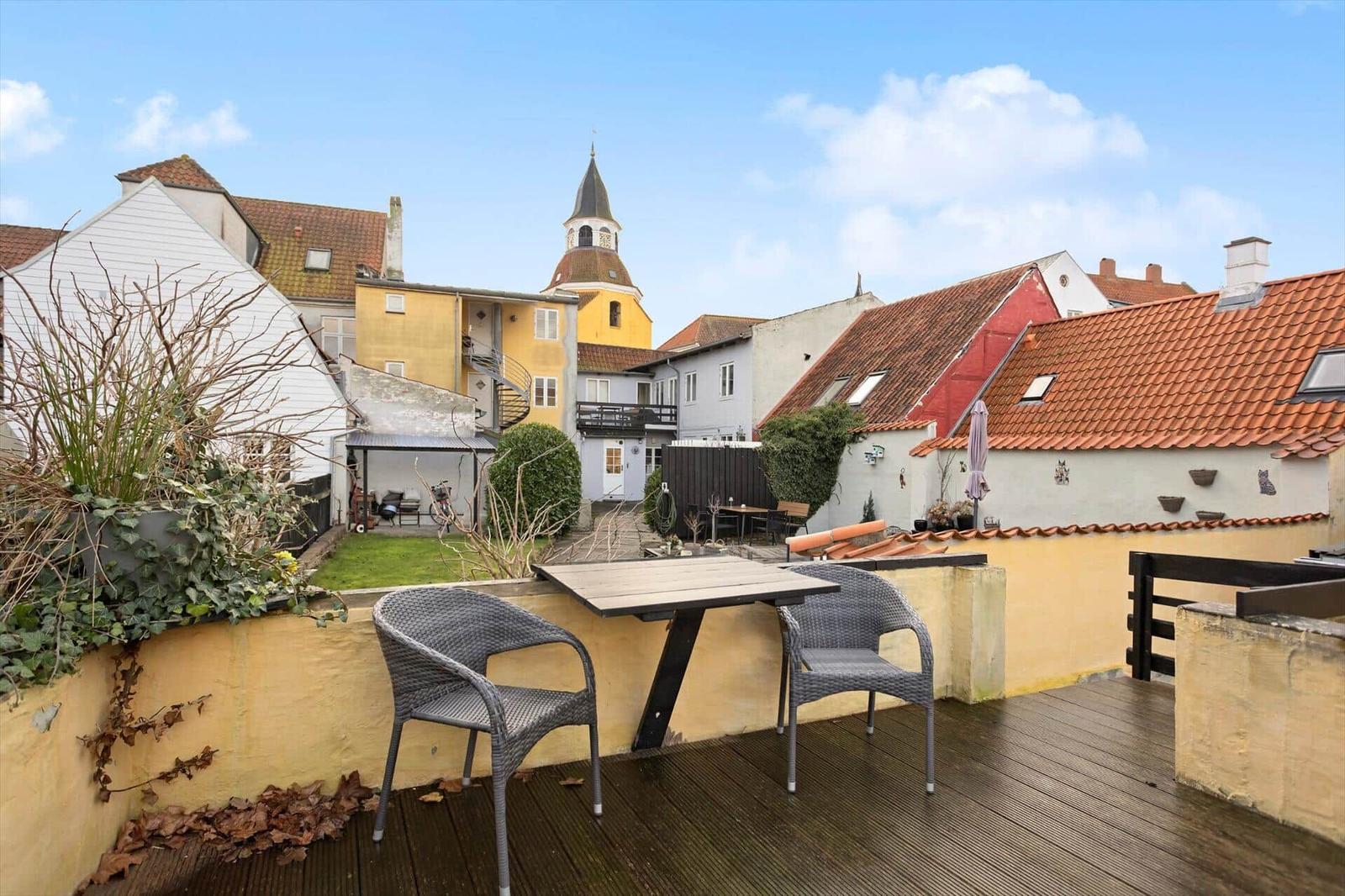 Terrace with table and chairs, view of roofs and tower.