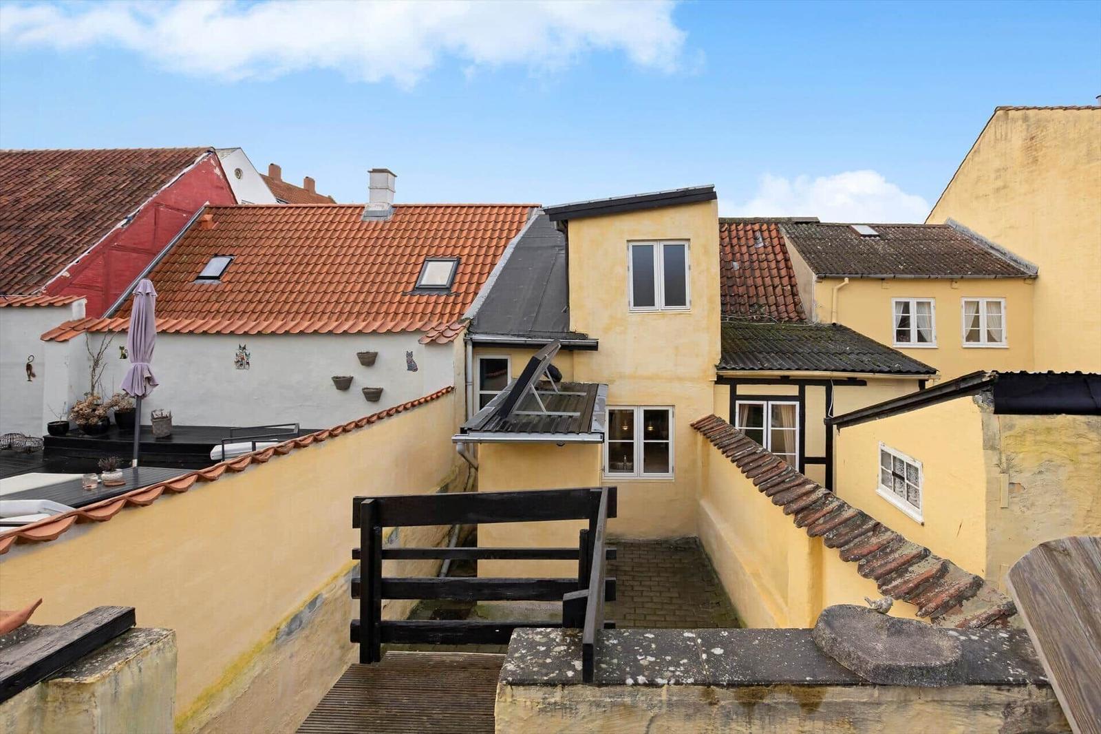Terrace with view of yellow buildings and red roofs under blue sky.
