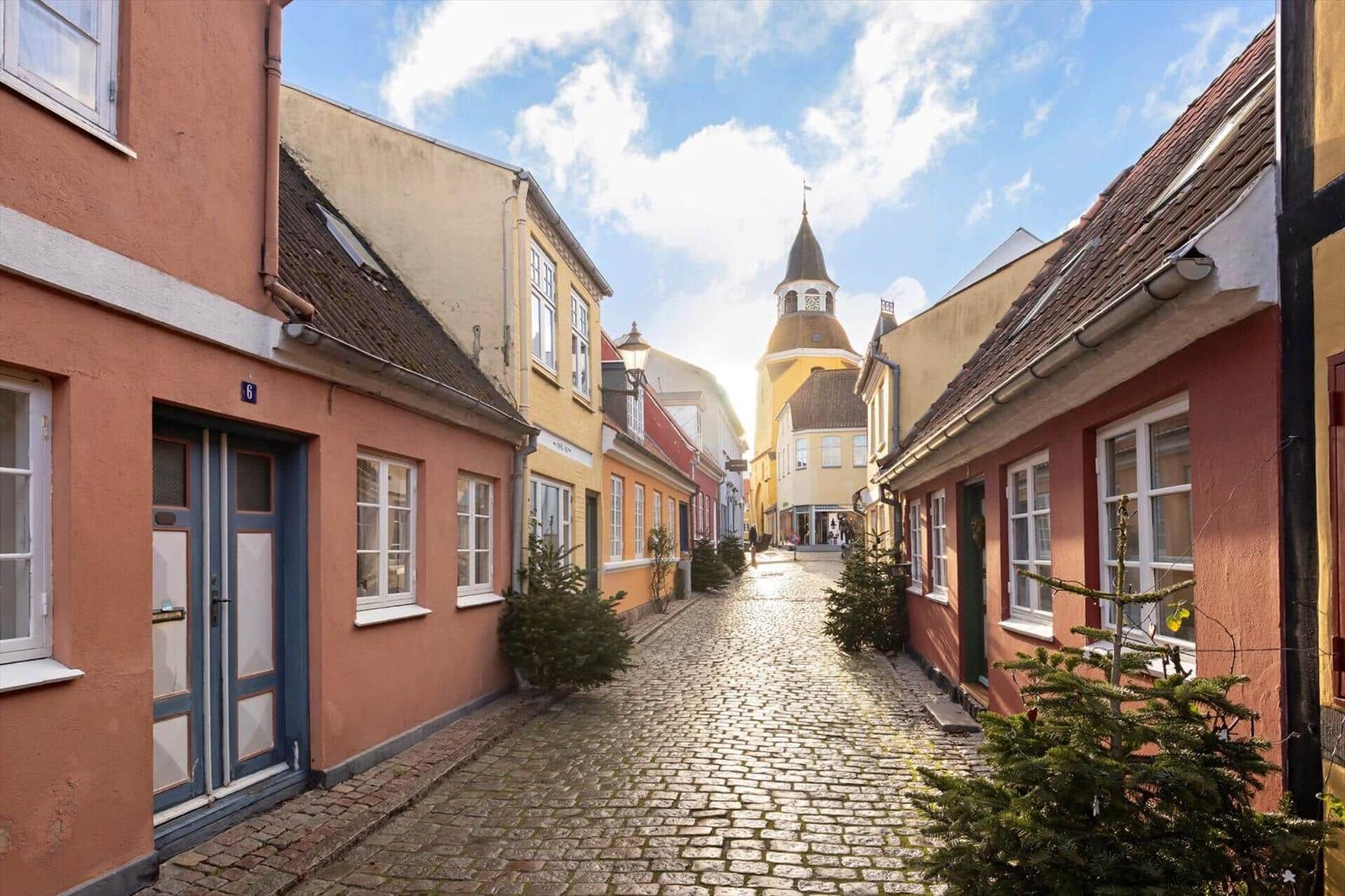 A cobblestone street with colorful houses and a tower in the background.