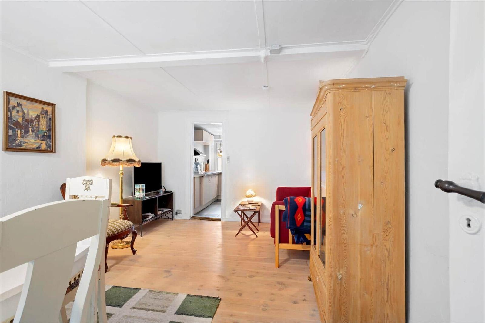Living room with wooden floor, wardrobe, and view into the kitchen.