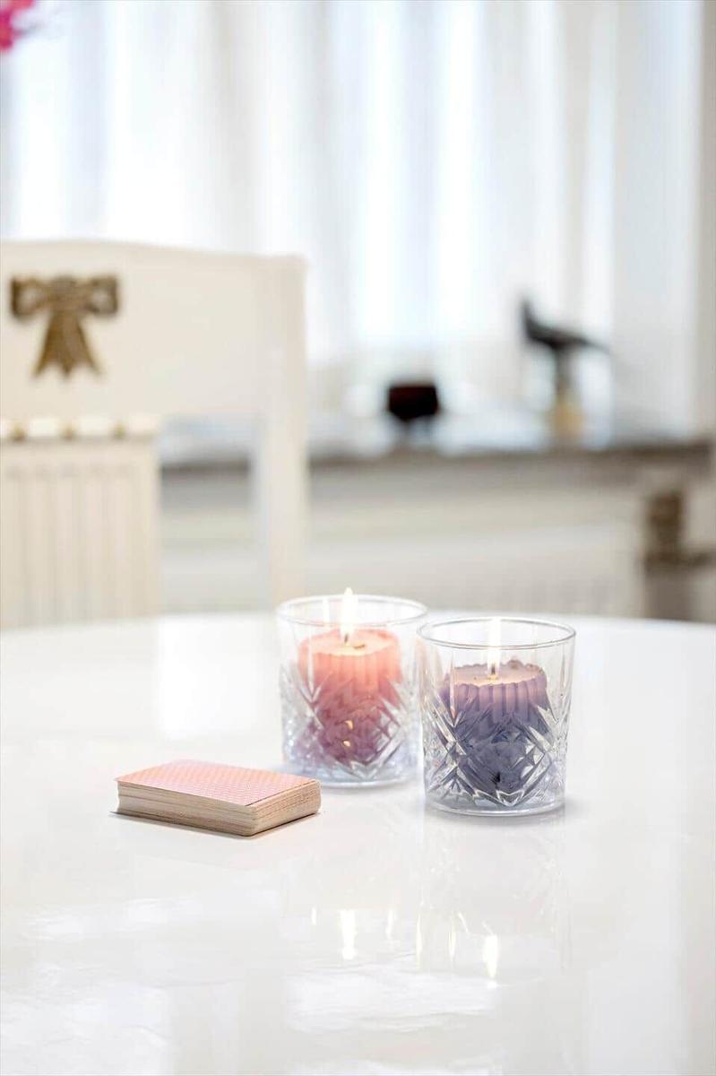 Two lit candles in glasses and a deck of cards are on the table.