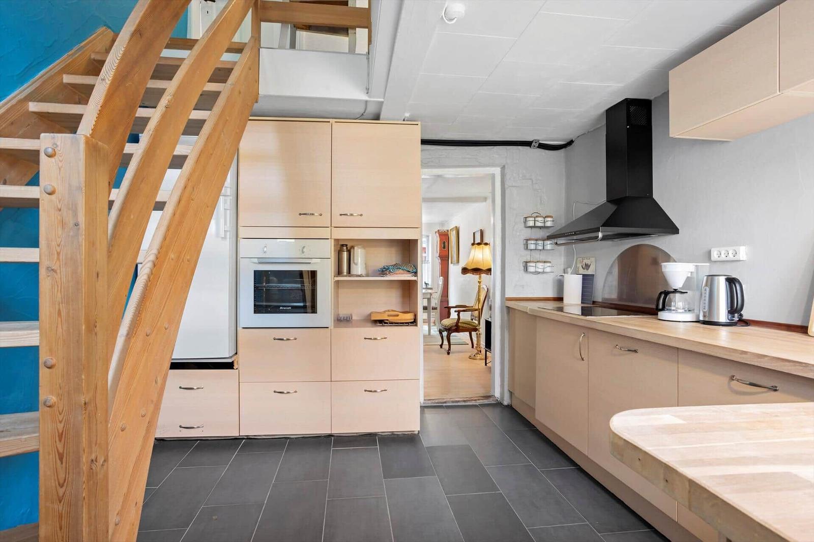 Kitchen with wooden cabinets, range hood, and kitchen island. Staircase on the left.