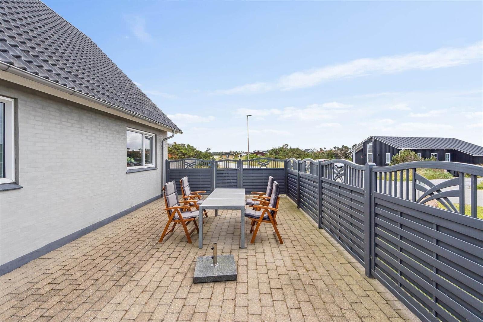 Terrasse mit Tisch und Stühlen, umgeben von einem Zaun. Hintergrund zeigt Häuser und Himmel.