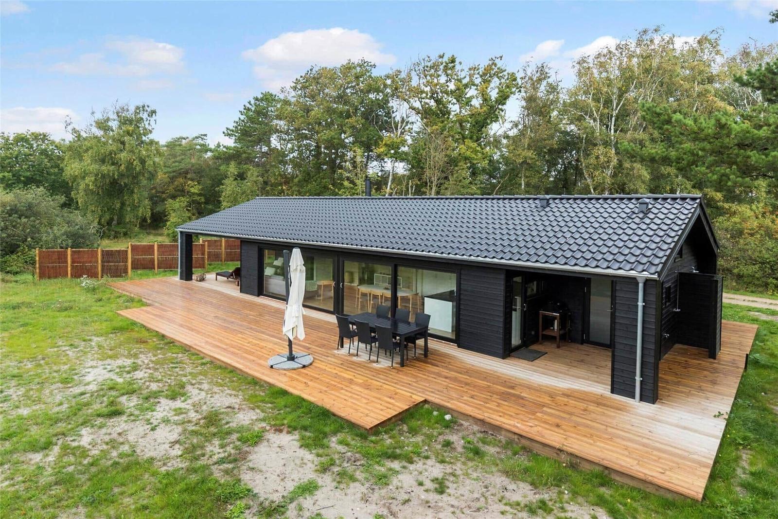 Modern cabin with wooden terrace, garden table, and view of forest.