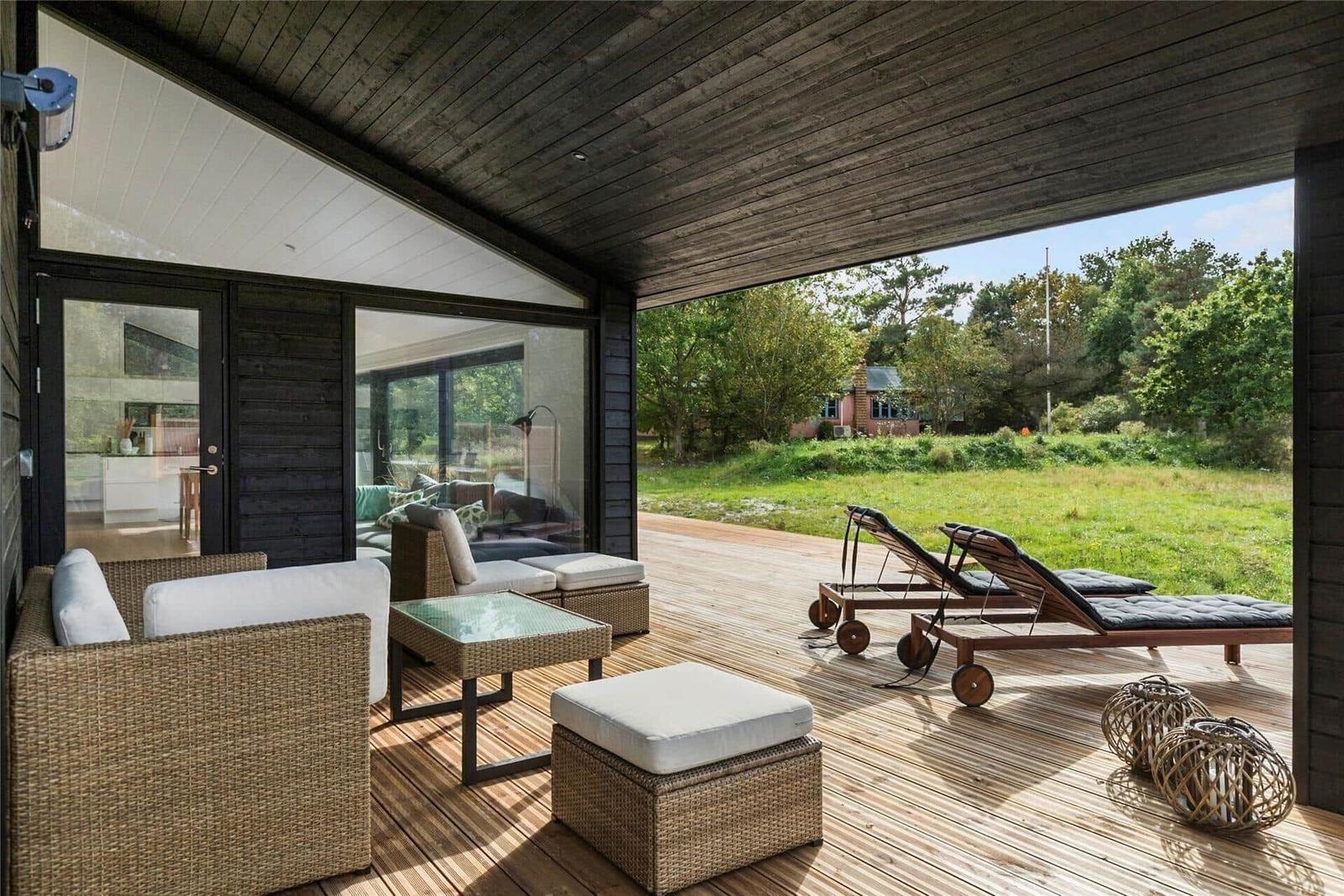 Deck with seating and loungers. View of green field and trees.