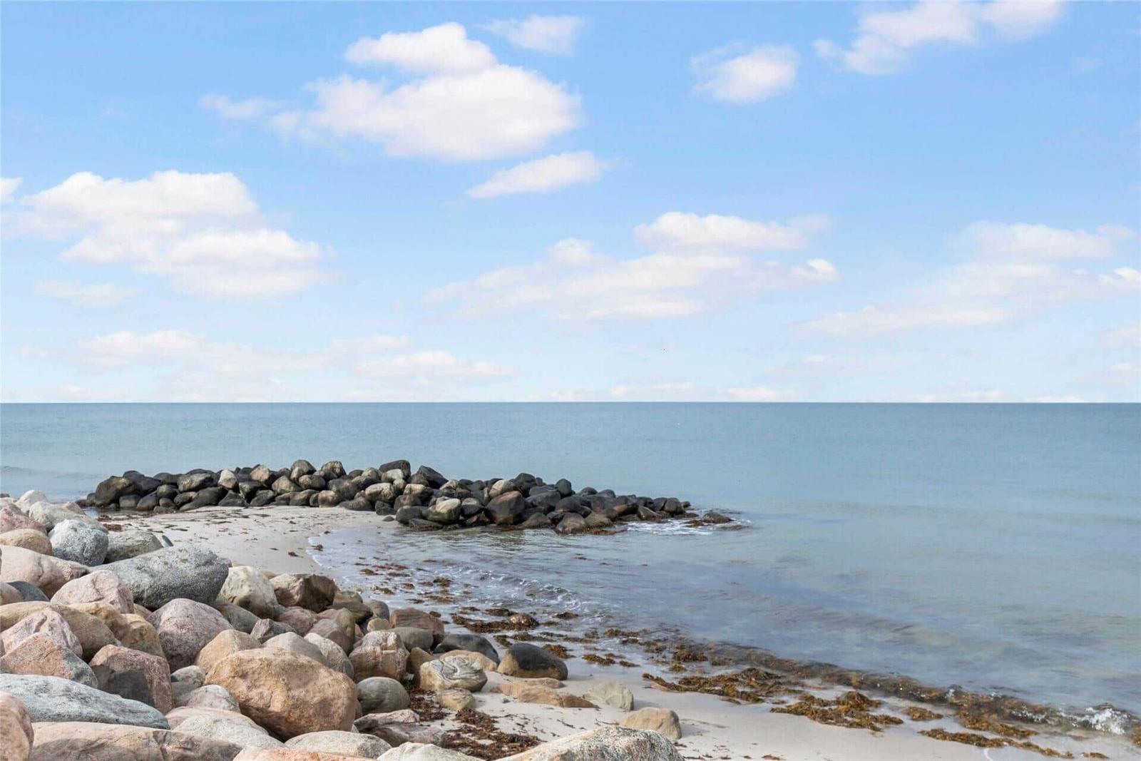 Beach with rocks and calm sea under blue sky with white clouds.