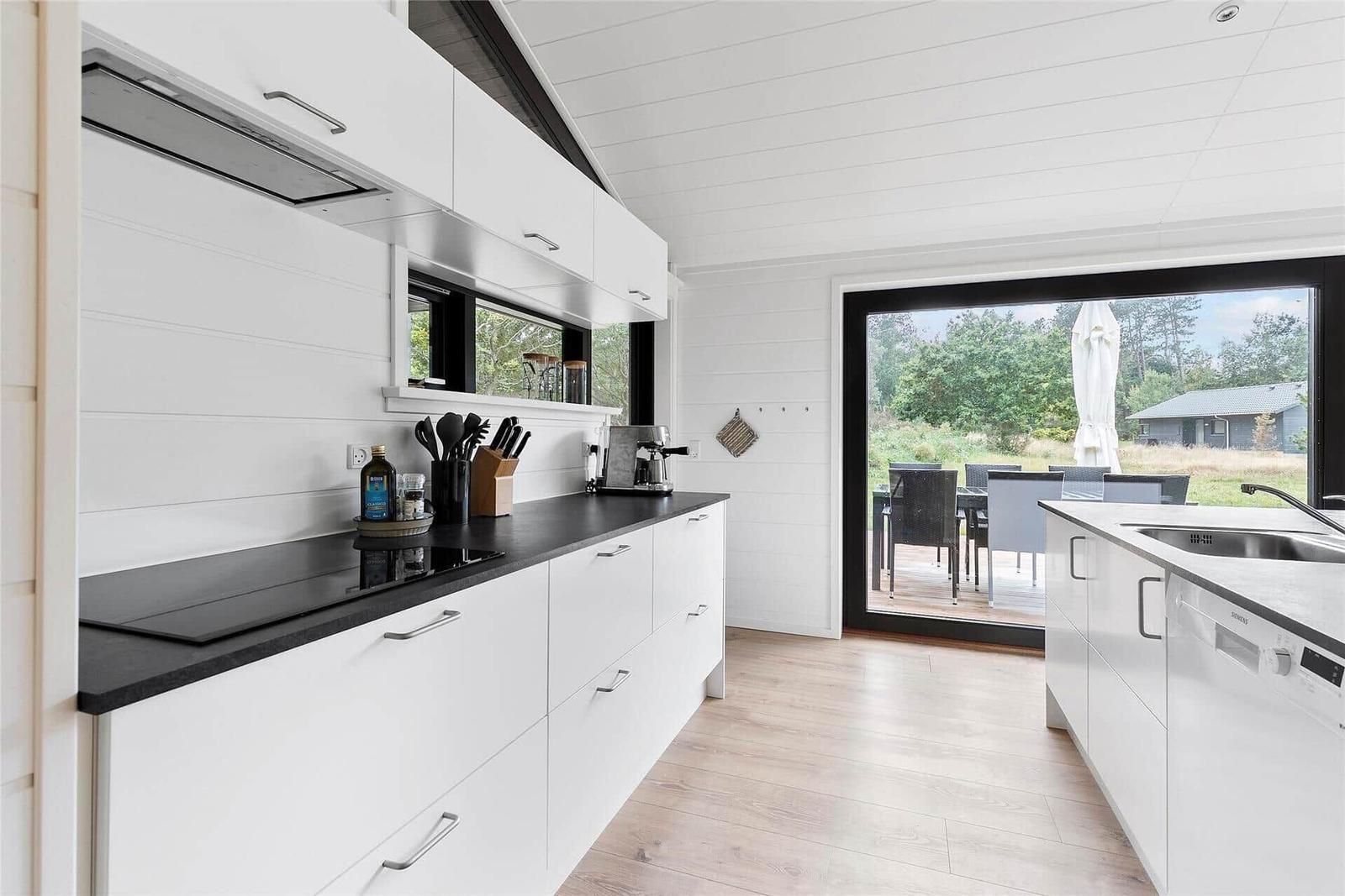 Kitchen with white cabinets, black countertop, and view to terrace with garden.