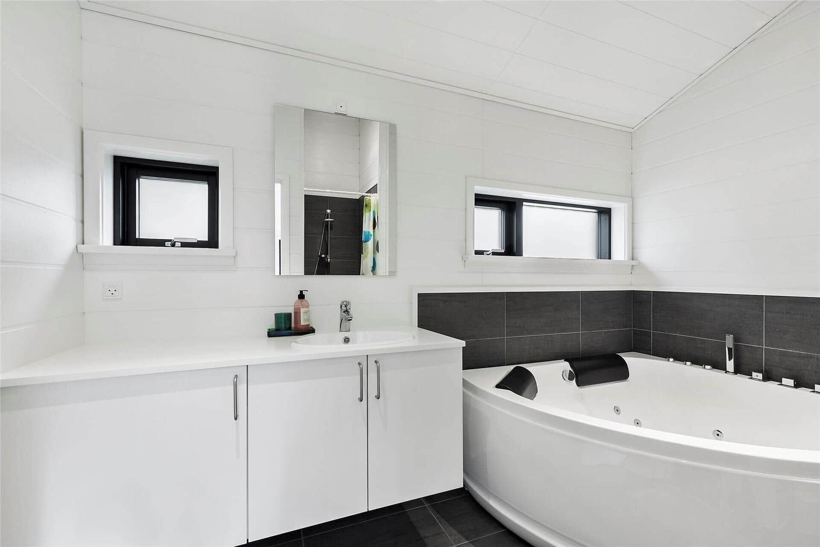 Bathroom with bathtub, sink, and mirror. White walls and black tiles.