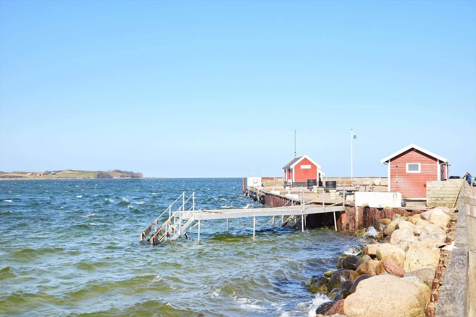 Harbor with red cabins and pier by the water. View of the coast in the background.