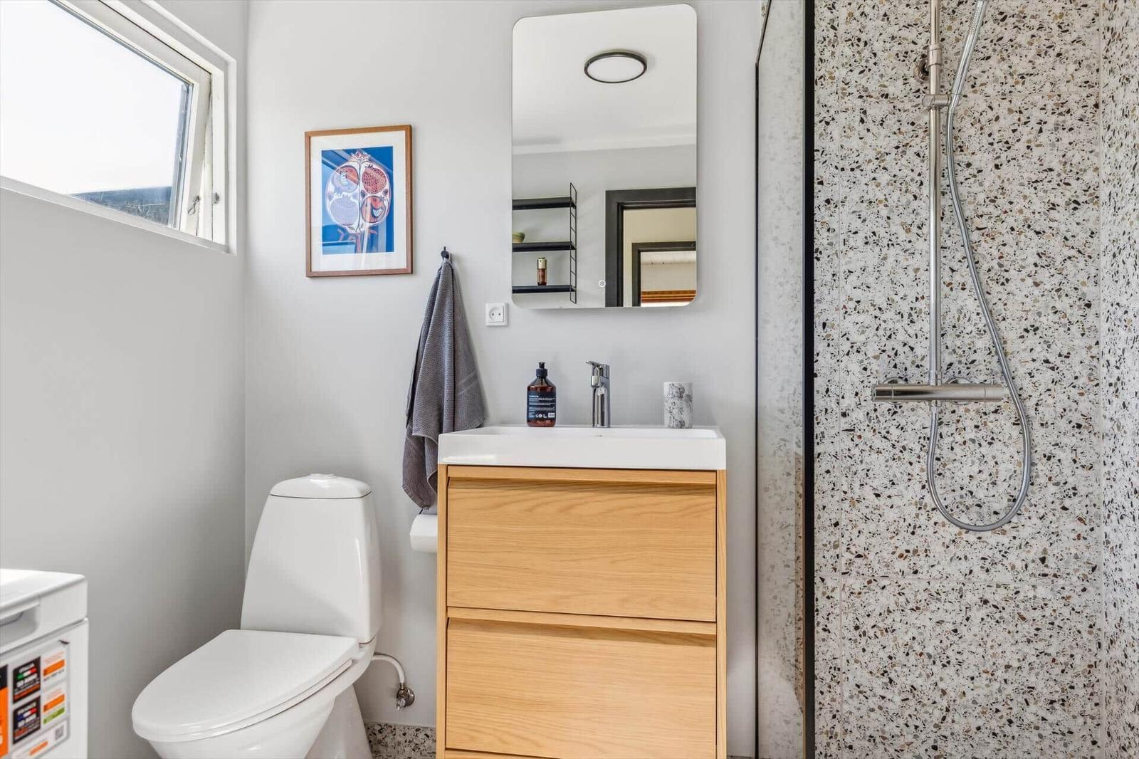 Bathroom with shower, sink, and toilet. Terrazzo tiles and wooden cabinet.