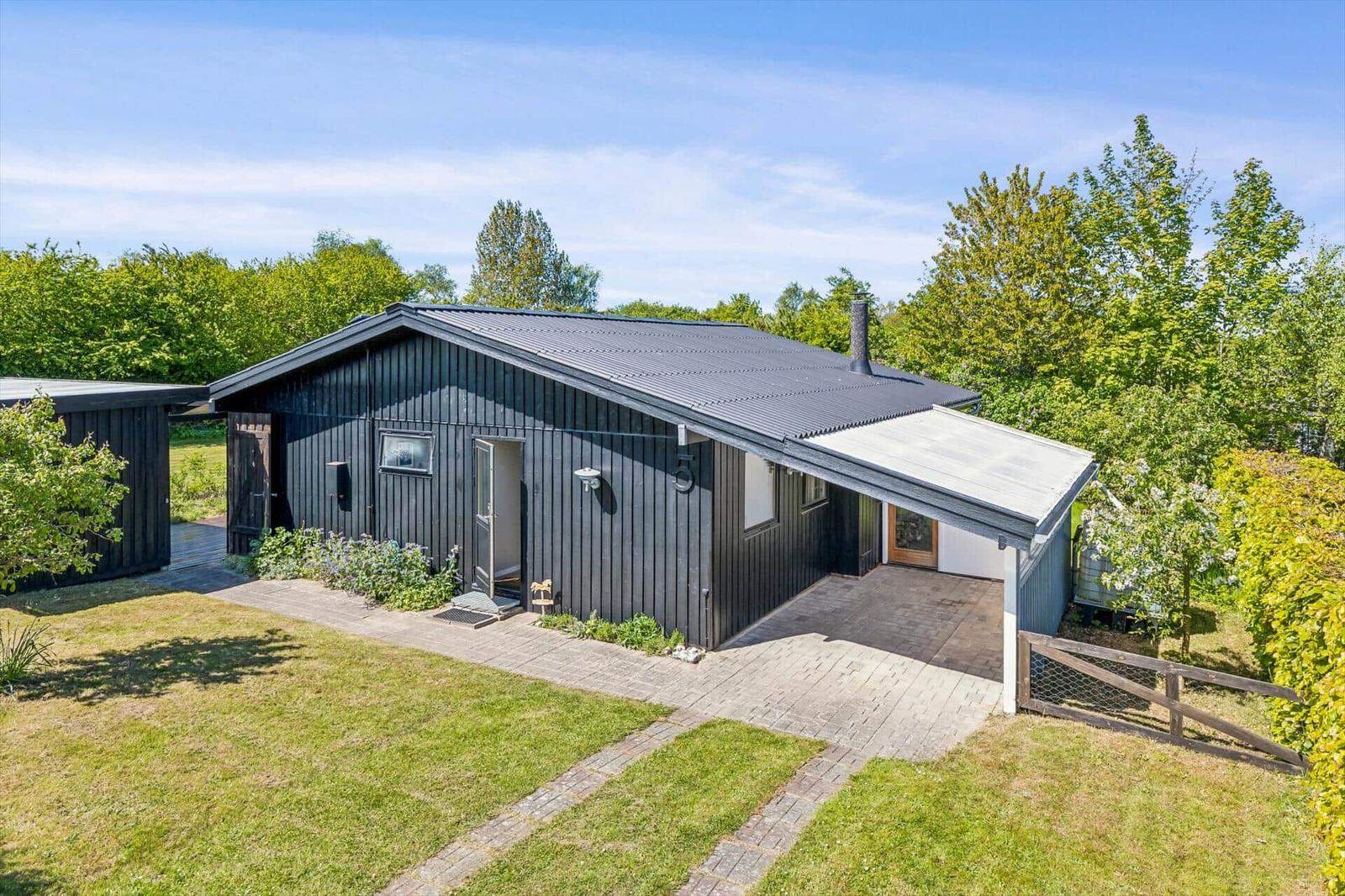Black wooden house with patio and garden. Surrounded by trees and greenery.