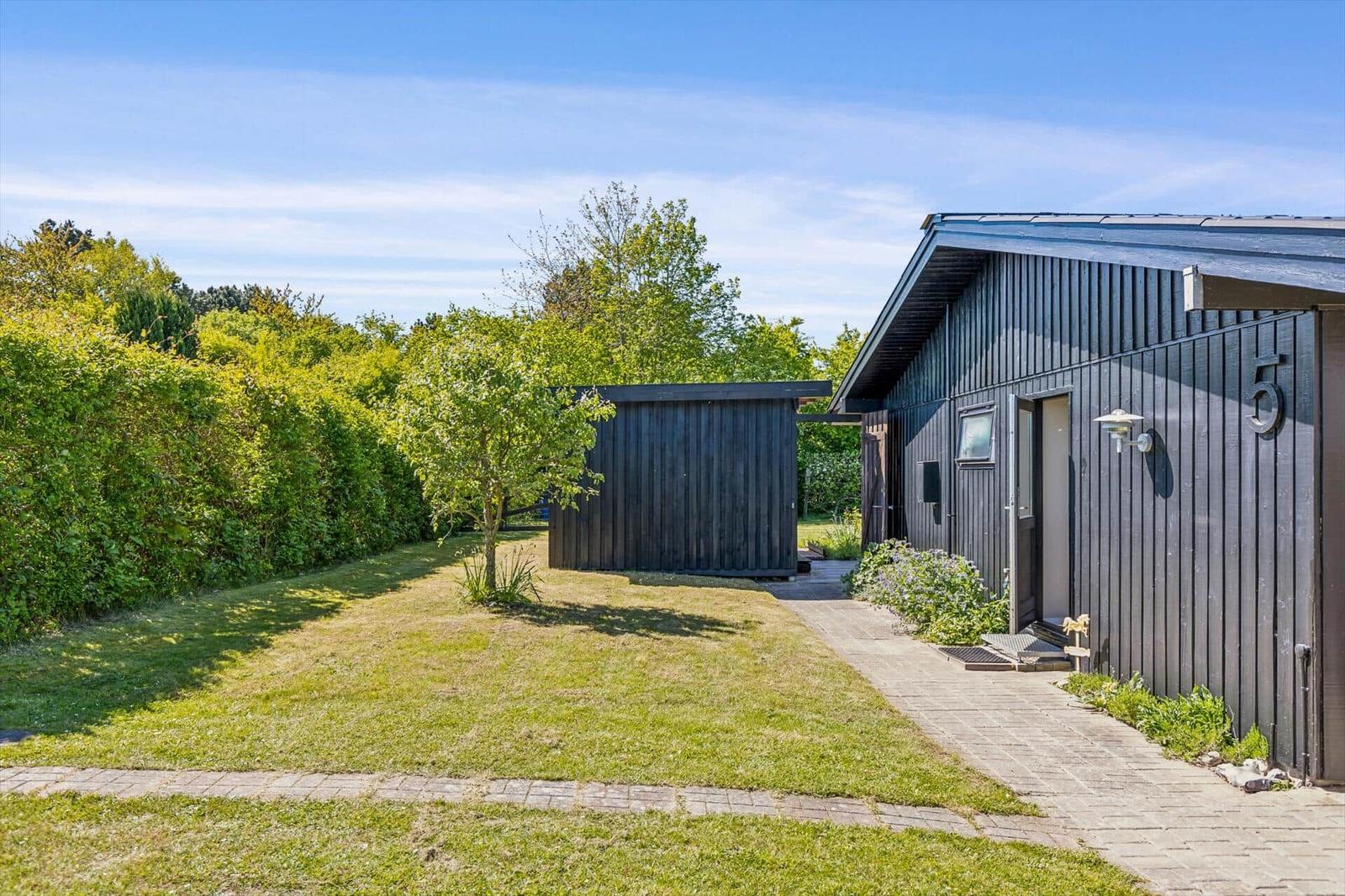 Black wooden house with garden, paved path, and small tree.