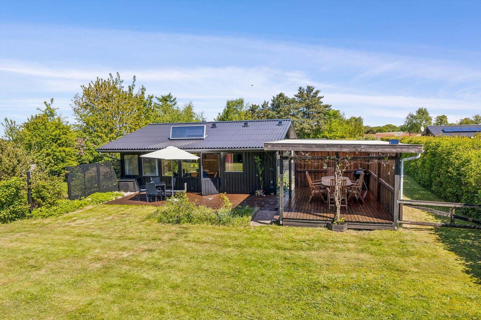 A house with a terrace and garden. On the terrace, there is a table with chairs and an umbrella.