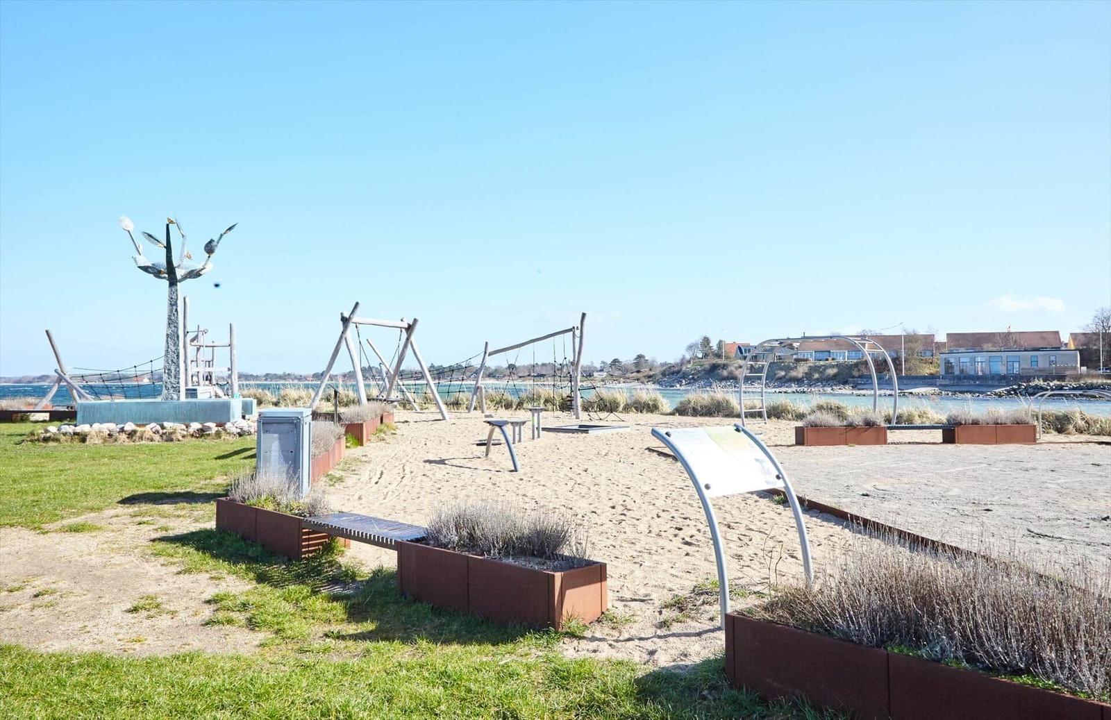 Sandy area with playground equipment and sculpture by water