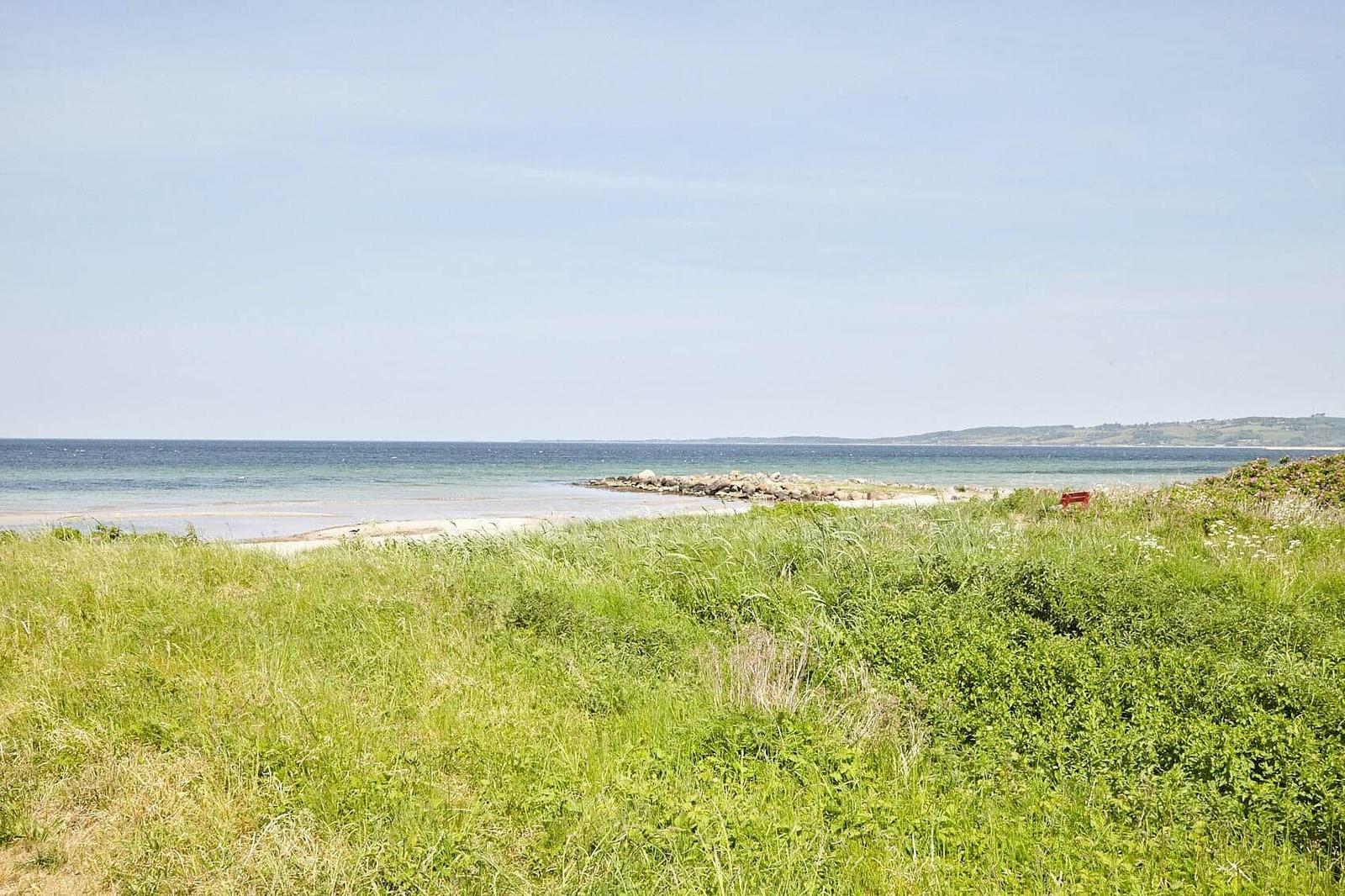 Green grass leads to a beach with a view of the sea and distant horizon.