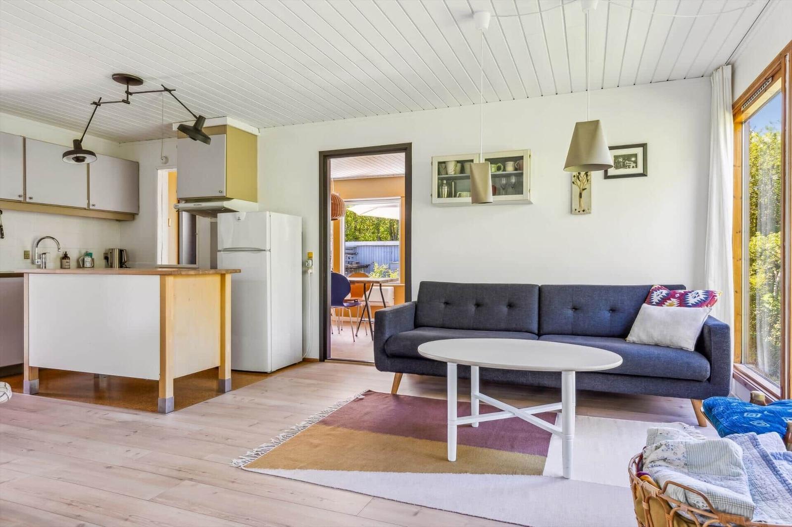 Living and kitchen area with sofa, table, and window. Kitchen with refrigerator and worktop.