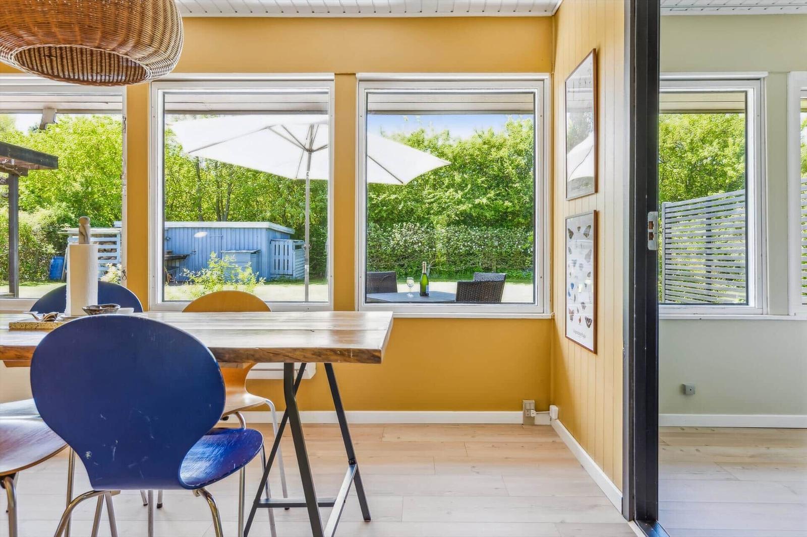 Dining room with wooden table and blue chairs, view of terrace with umbrella.
