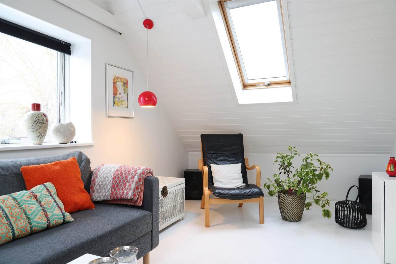 Living room with sofa, armchair, plant, and windows. White walls and ceiling.