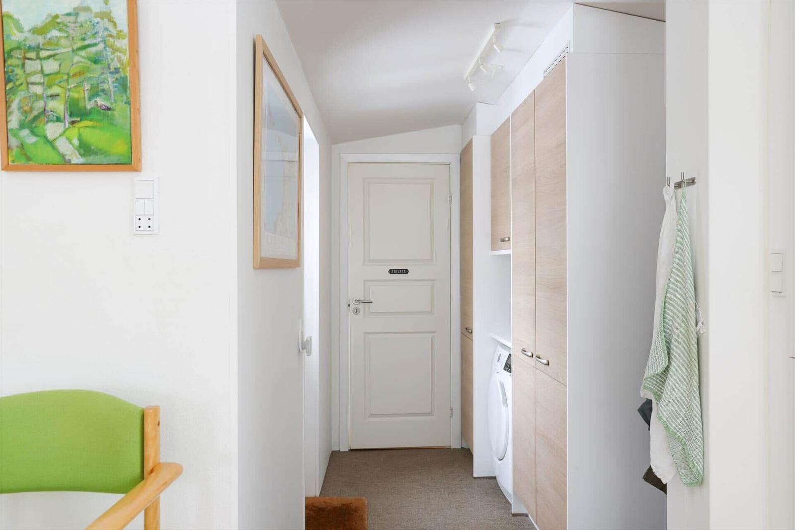 Hallway with wardrobe, washing machine, and door to bathroom. Green seating and wall art.