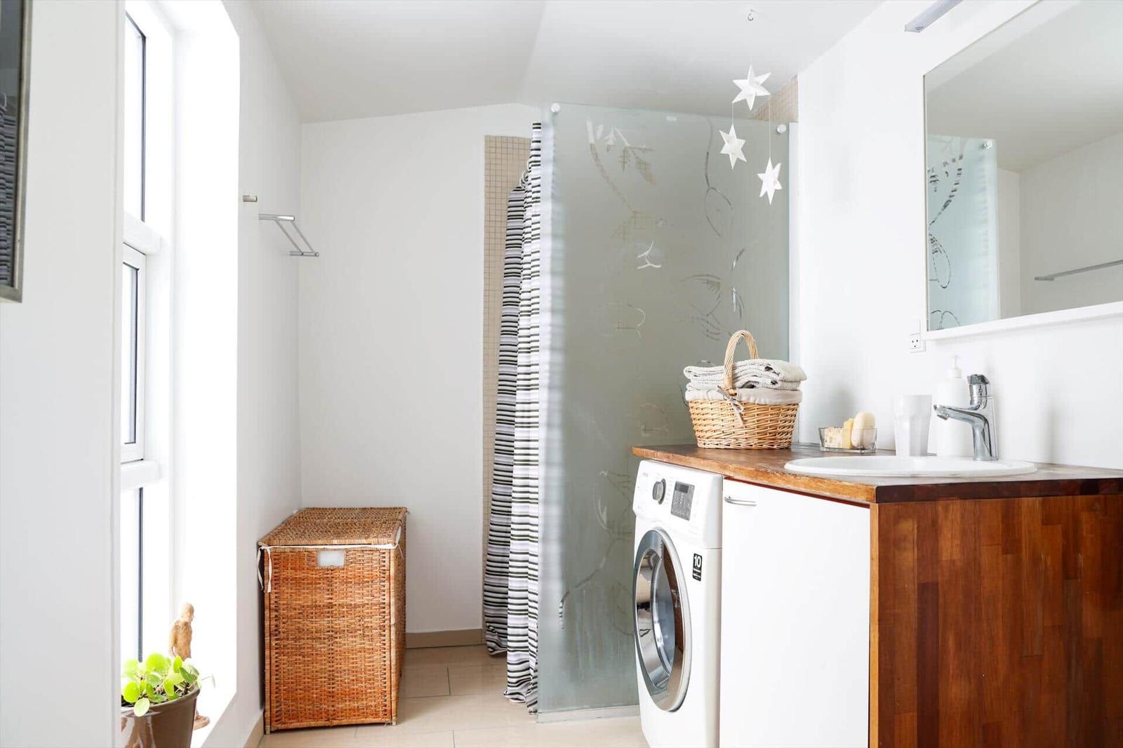 Bathroom with washing machine, sink, and shower with glass partition.