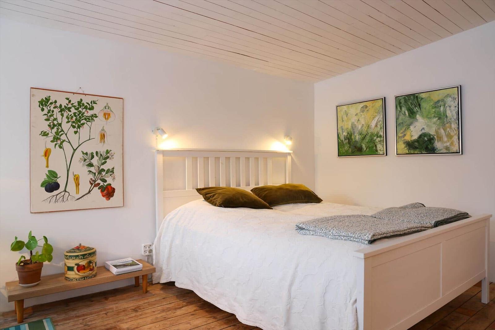 Bedroom with white bed, wooden floor, and wall art.