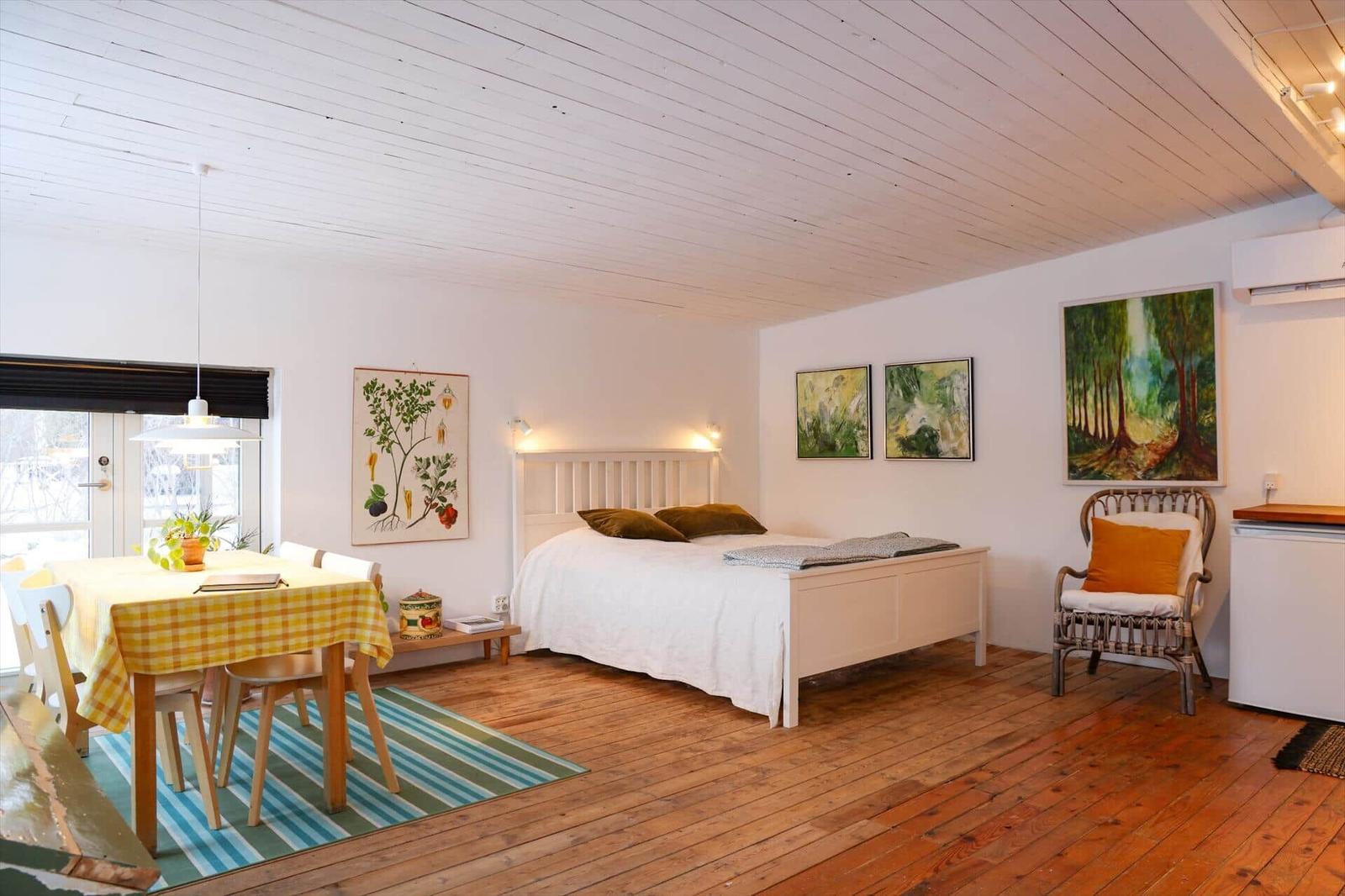 Bedroom with bed, chair, and dining table. Wooden floor and white walls.