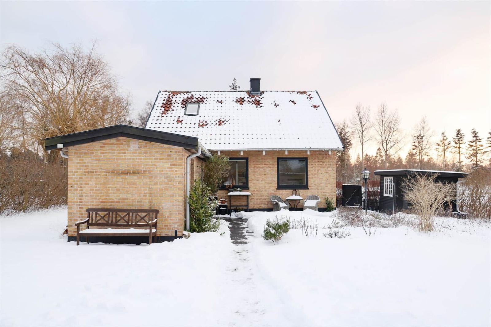 Winter cottage with snow-covered roof, wooden bench, and garden furniture.