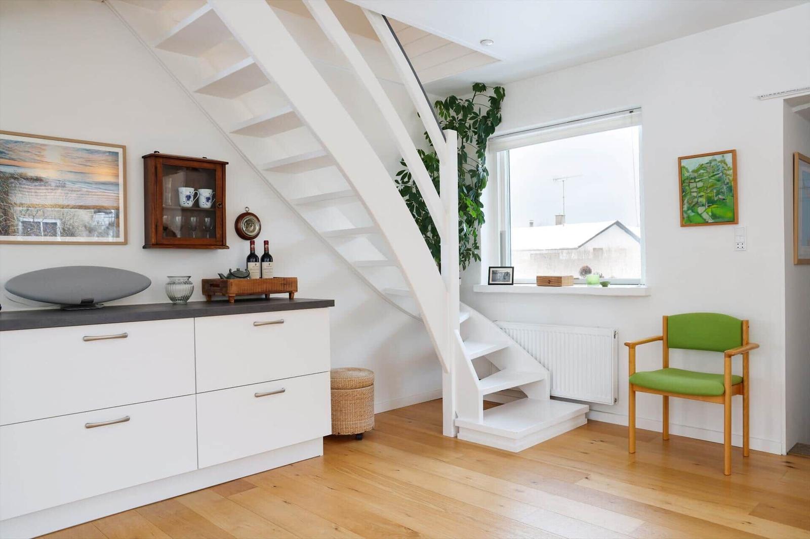 Living area with white stairs, green seating, and wooden floor.