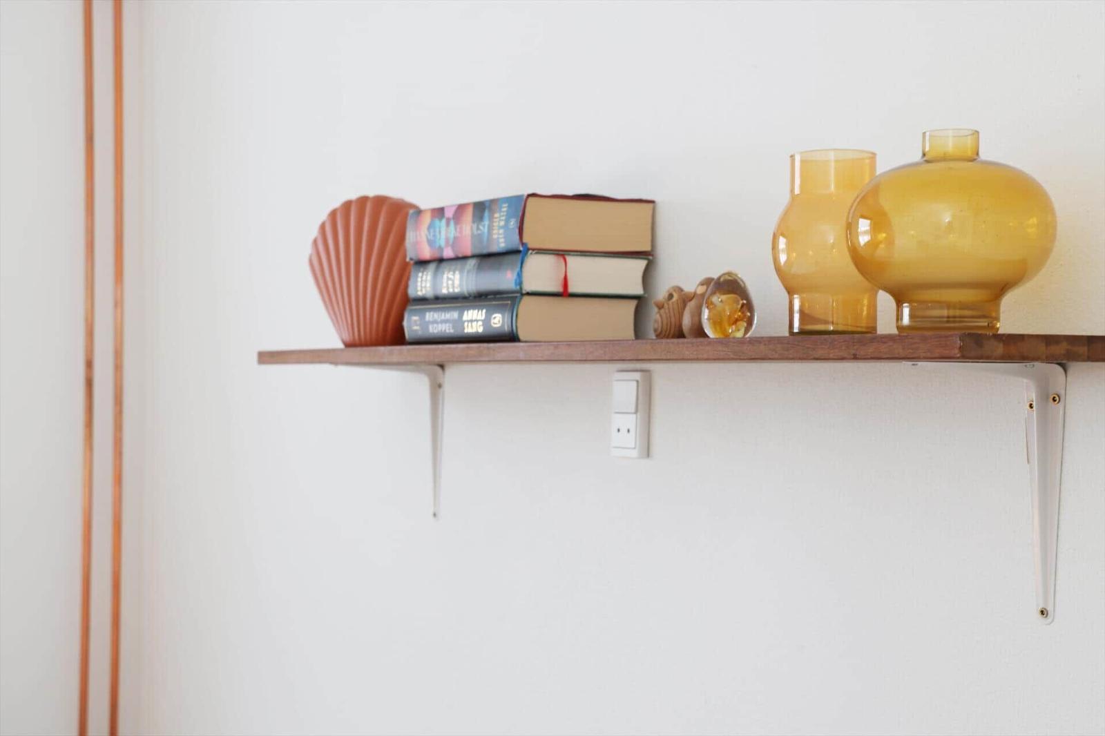 Wooden shelf on the wall with books, vase, and shell.