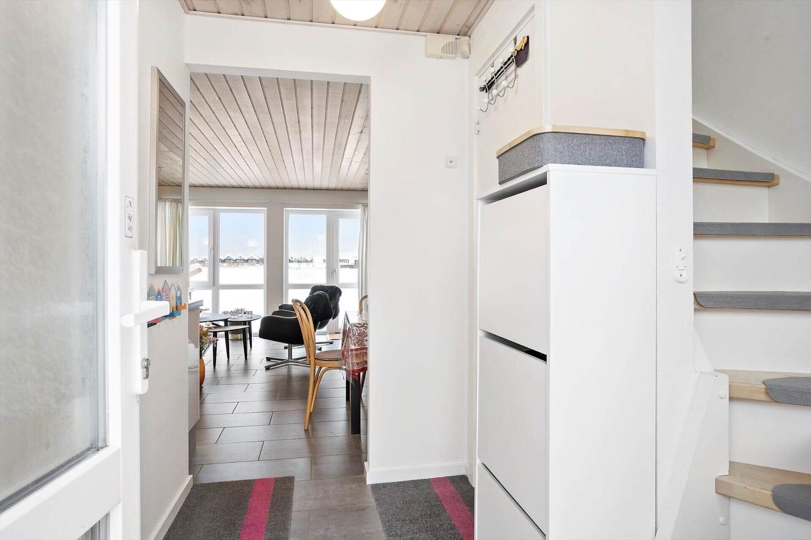 Hallway with stairs, storage, and view into living area with windows.