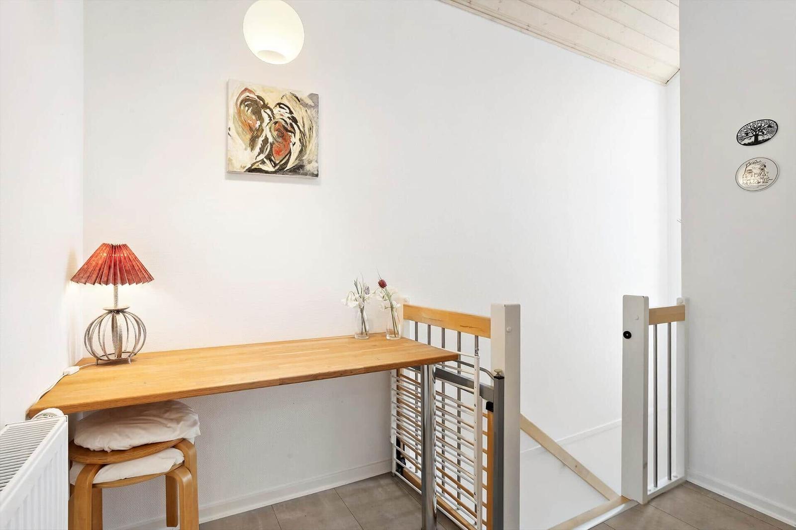 Wooden desk with chair, lamp, and flowers. Wall art and gate visible.