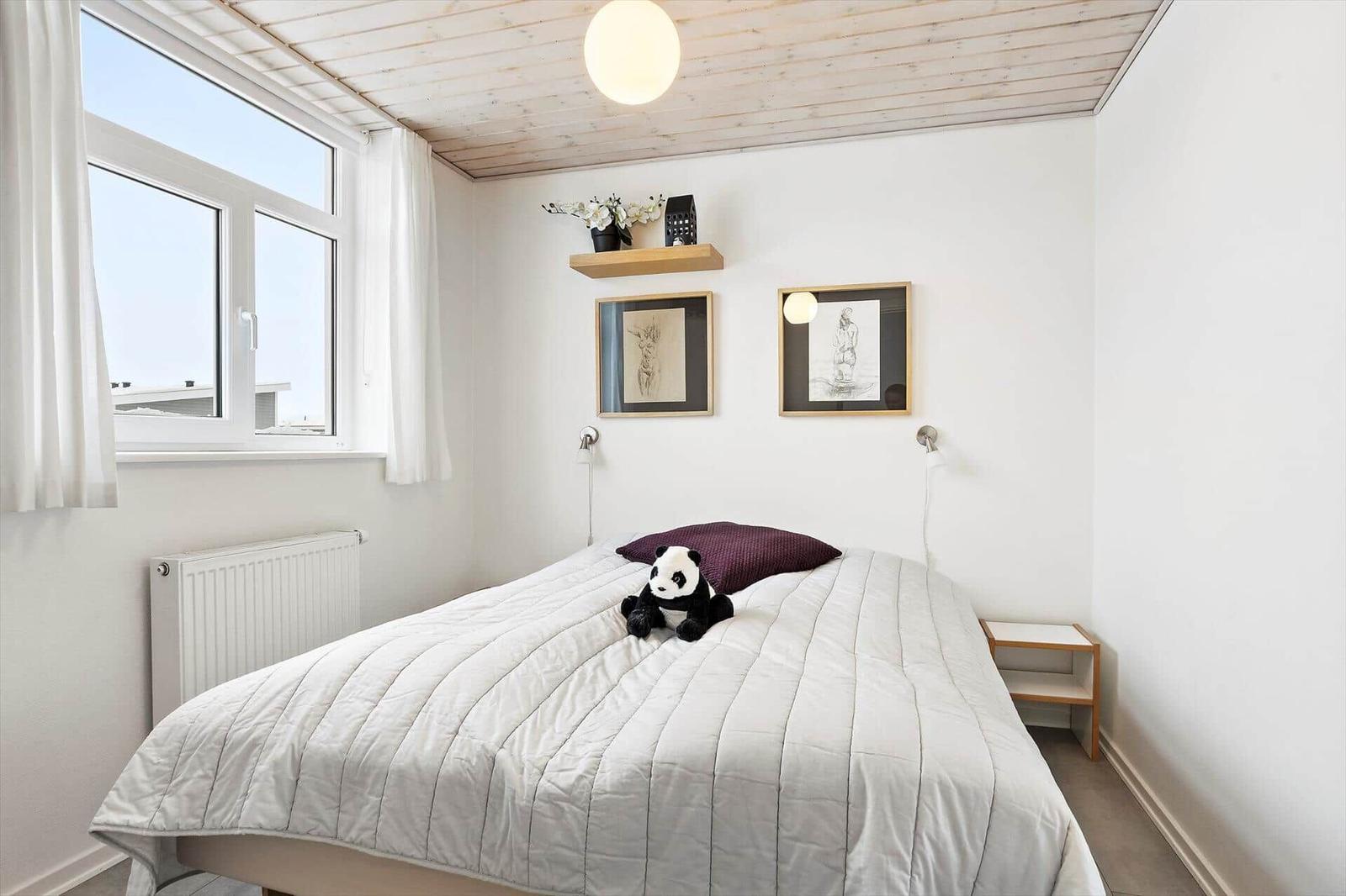 Bedroom with bed, window, wall art, and wall lamp.