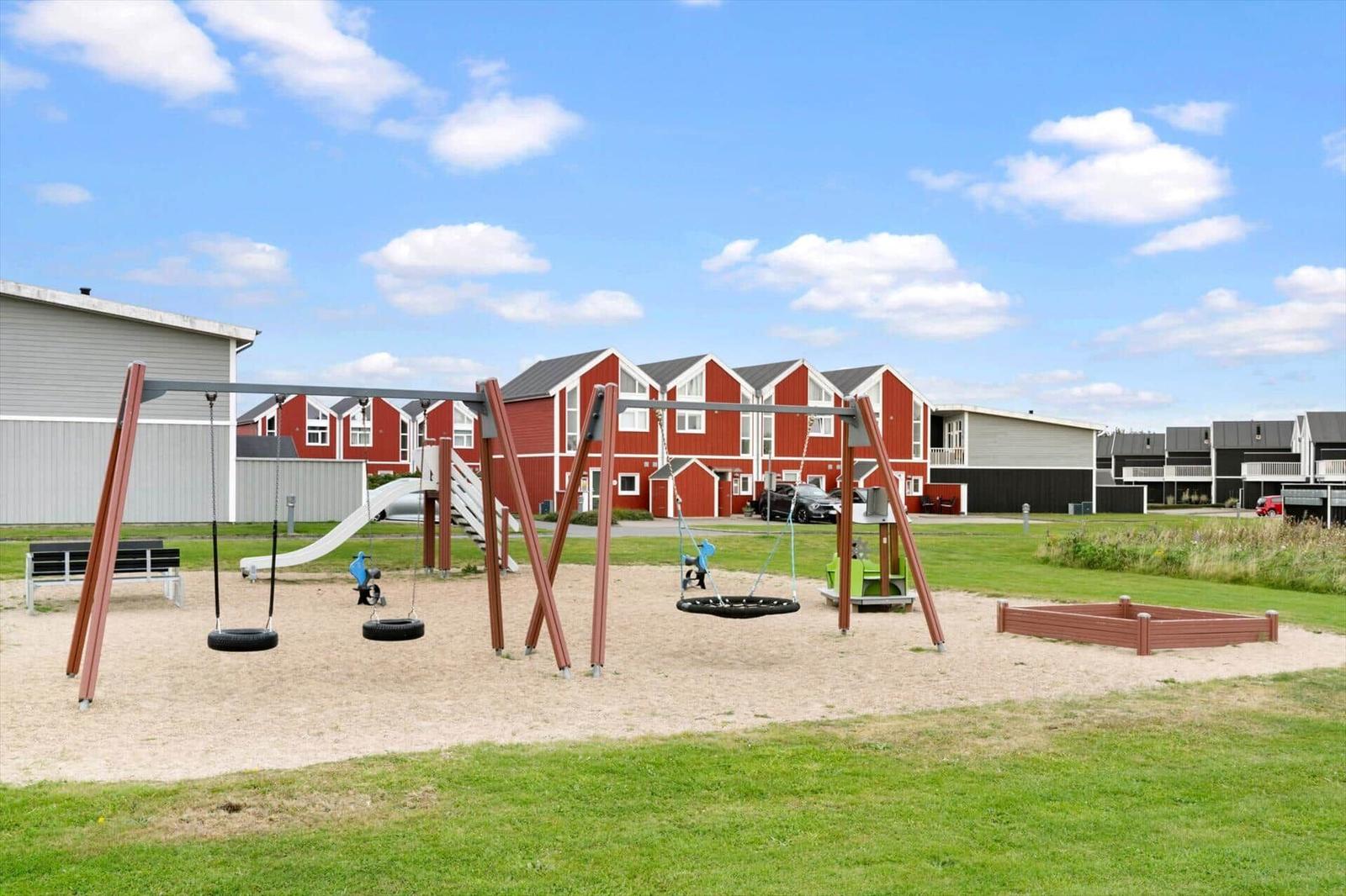 Play area with swings, sandbox, and slide in front of red holiday homes.